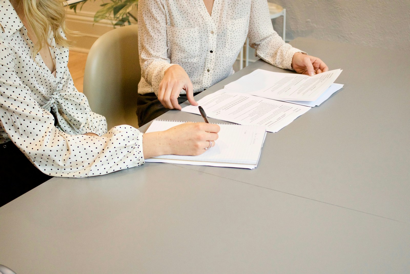 Two women reviewing documents together at a table, faces not shown