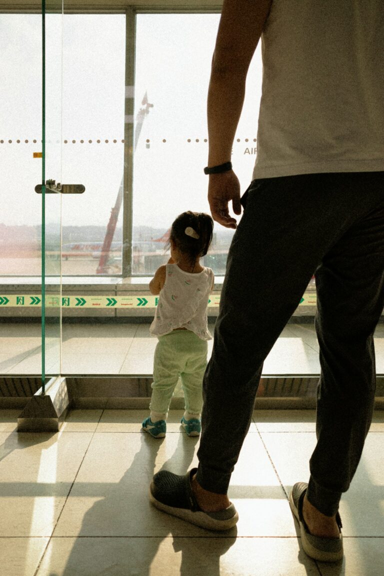 A parent and a young child seen from behind, looking out of an airport window